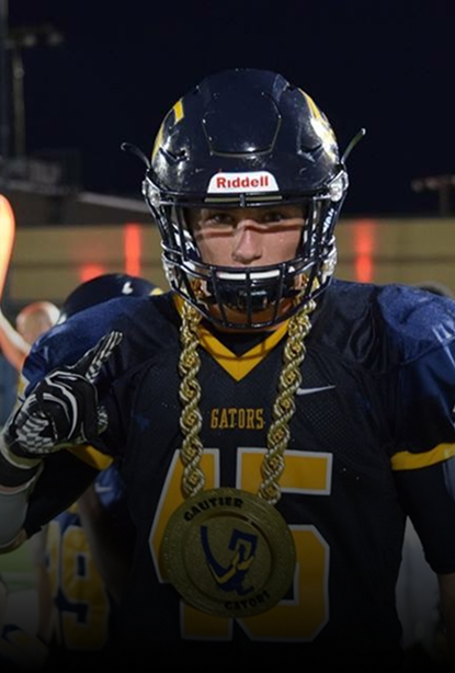 A football player in a navy and yellow uniform with a large gold chain medallion around his neck